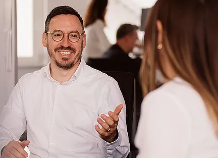 Zwei Arbeitskollegen unterhalten sich am Schreibtisch.