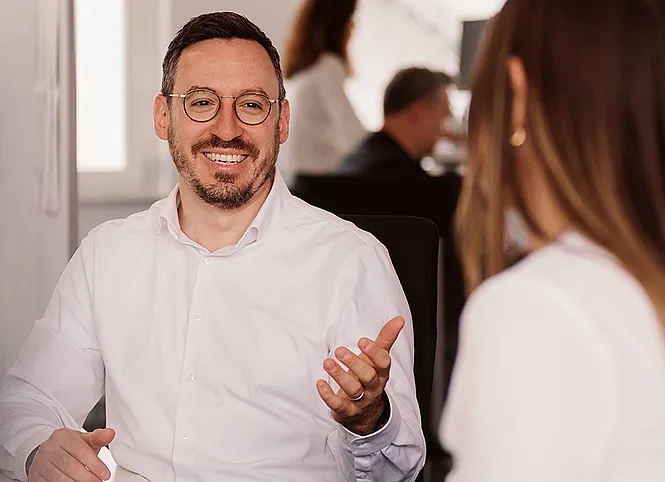 Zwei Arbeitskollegen unterhalten sich am Schreibtisch.