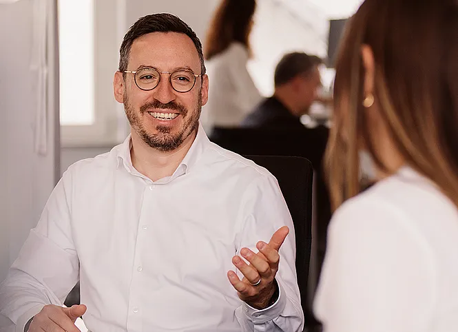 Two colleagues are talking at their desks.