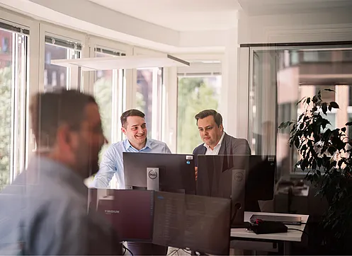 Zwei Kollegen sitzen am Bildschirm und unterhalten sich.